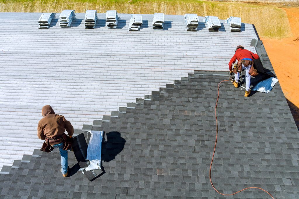 Aerial view in worker hands installing bitumen roof shingles with air hammer and nail