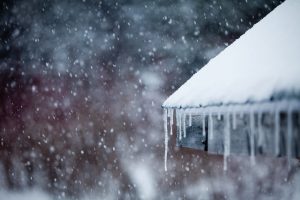 Snow-covered roof with hanging icicles during a winter snowfall.