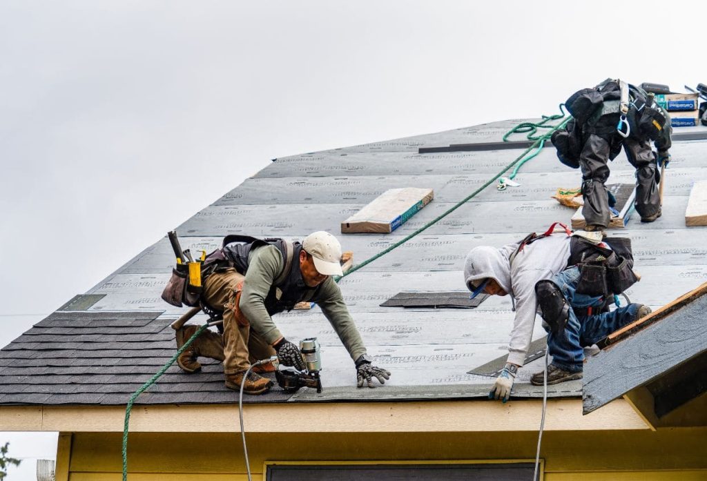 Roofing professional wearing a safety helmet and working on a sloped clay tile roof, inspecting or repairing the roof near a ridge.