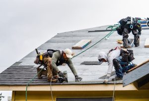 Roofing professional wearing a safety helmet and working on a sloped clay tile roof, inspecting or repairing the roof near a ridge.
